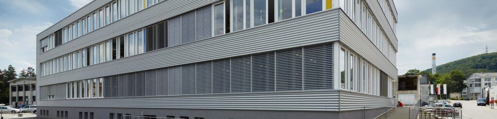 Modernes Buerogebaeude mit silbriger Wellblechfassade und Sonnenstoren
