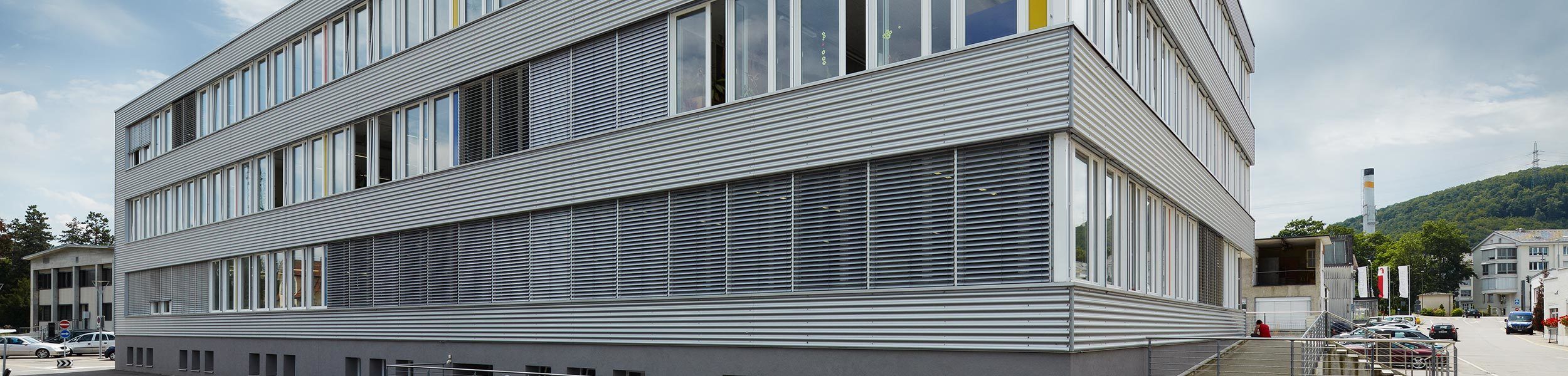 Modernes Buerogebaeude mit silbriger Wellblechfassade und Sonnenstoren